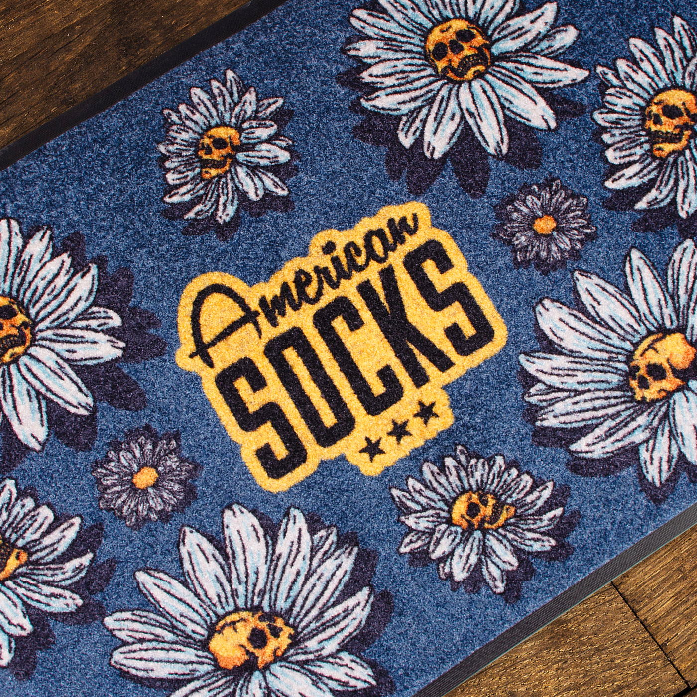 Close up of floral patterned rug with punk daisy flowers with skull in the middle design and american socks logo in the center 