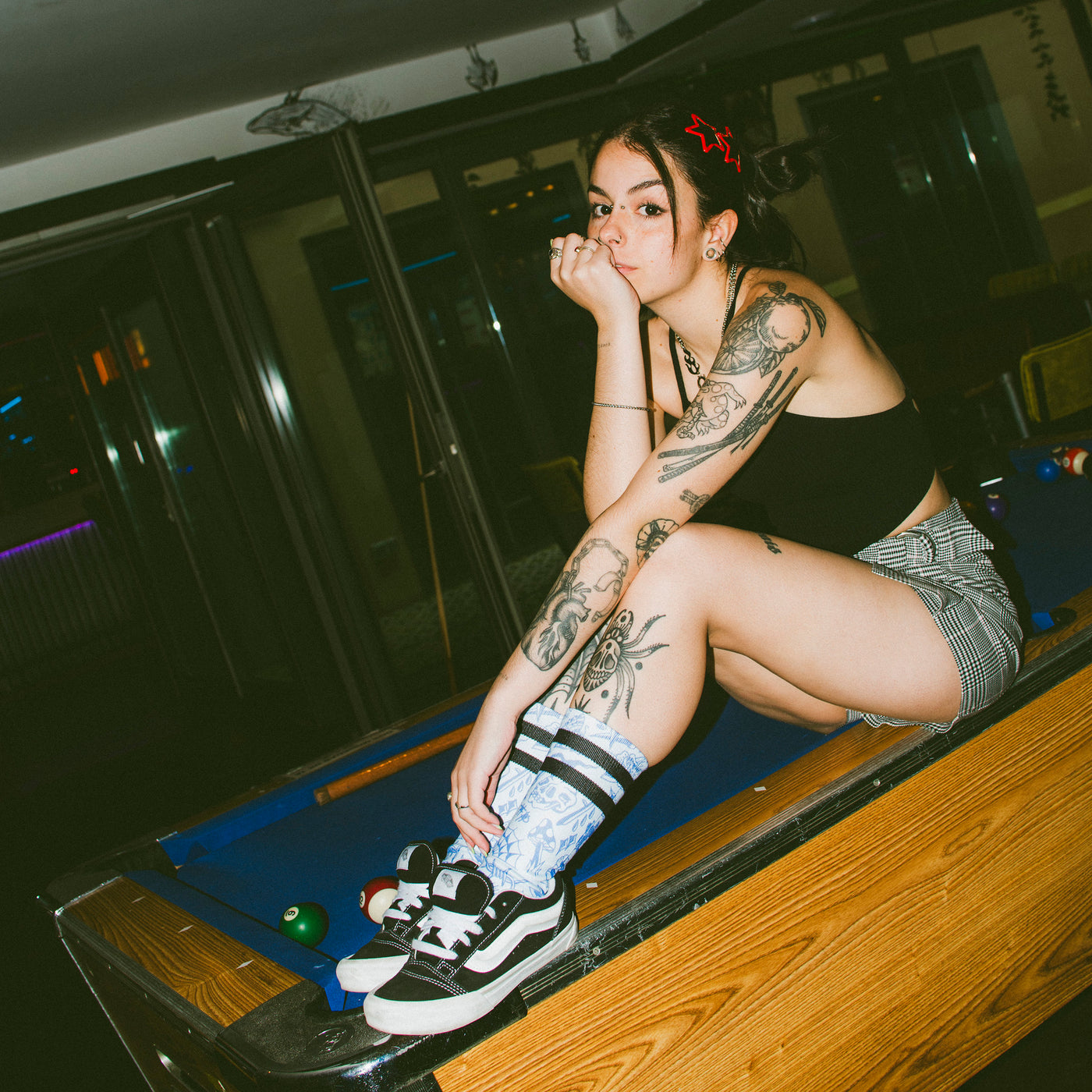 Alternative woman sitting on pool table wearing blue 80s tattoo inspired skate socks american socks